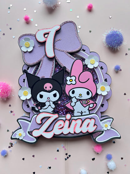 Decorative cake topper with cartoon characters and decorative elements on a light pink background