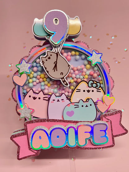 Decorative cake topper with cartoon cats, colorful text, and a rainbow design on a pink background.