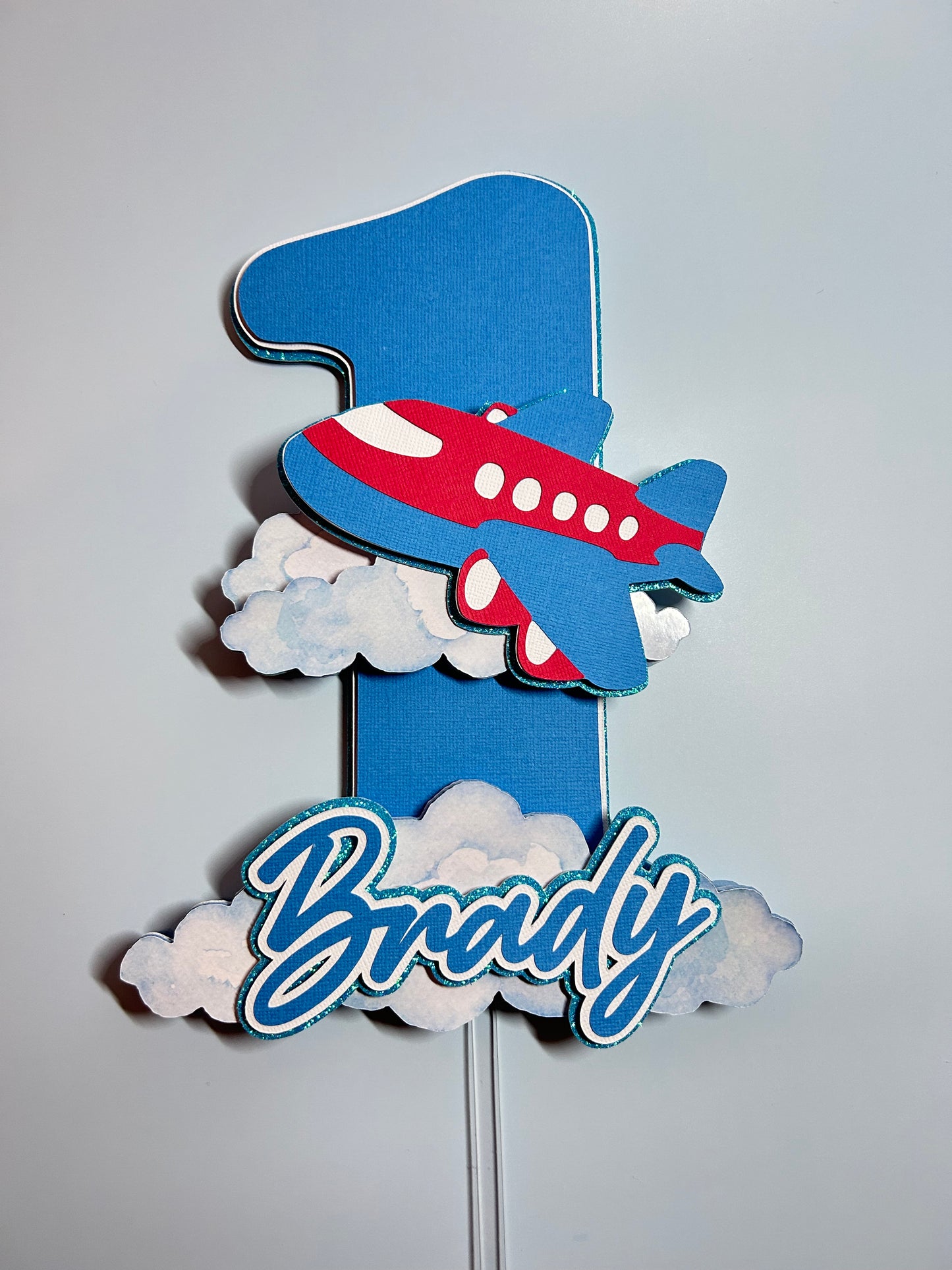 Decorative airplane and clouds cake topper with 'Happy Birthday' text on a light gray background