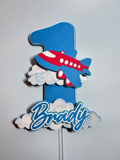 Decorative airplane and clouds cake topper with 'Happy Birthday' text on a light gray background