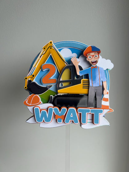 Colorful construction-themed cake topper with an excavator, worker, and 'Wyatt' text on a gray background.