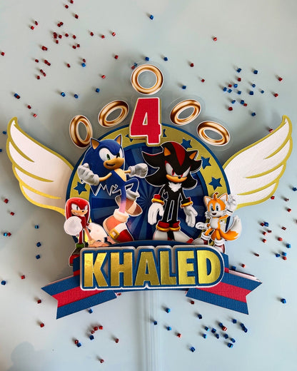 Personalized birthday cake topper with cartoon characters and 'Khaled' text on a light gray background.