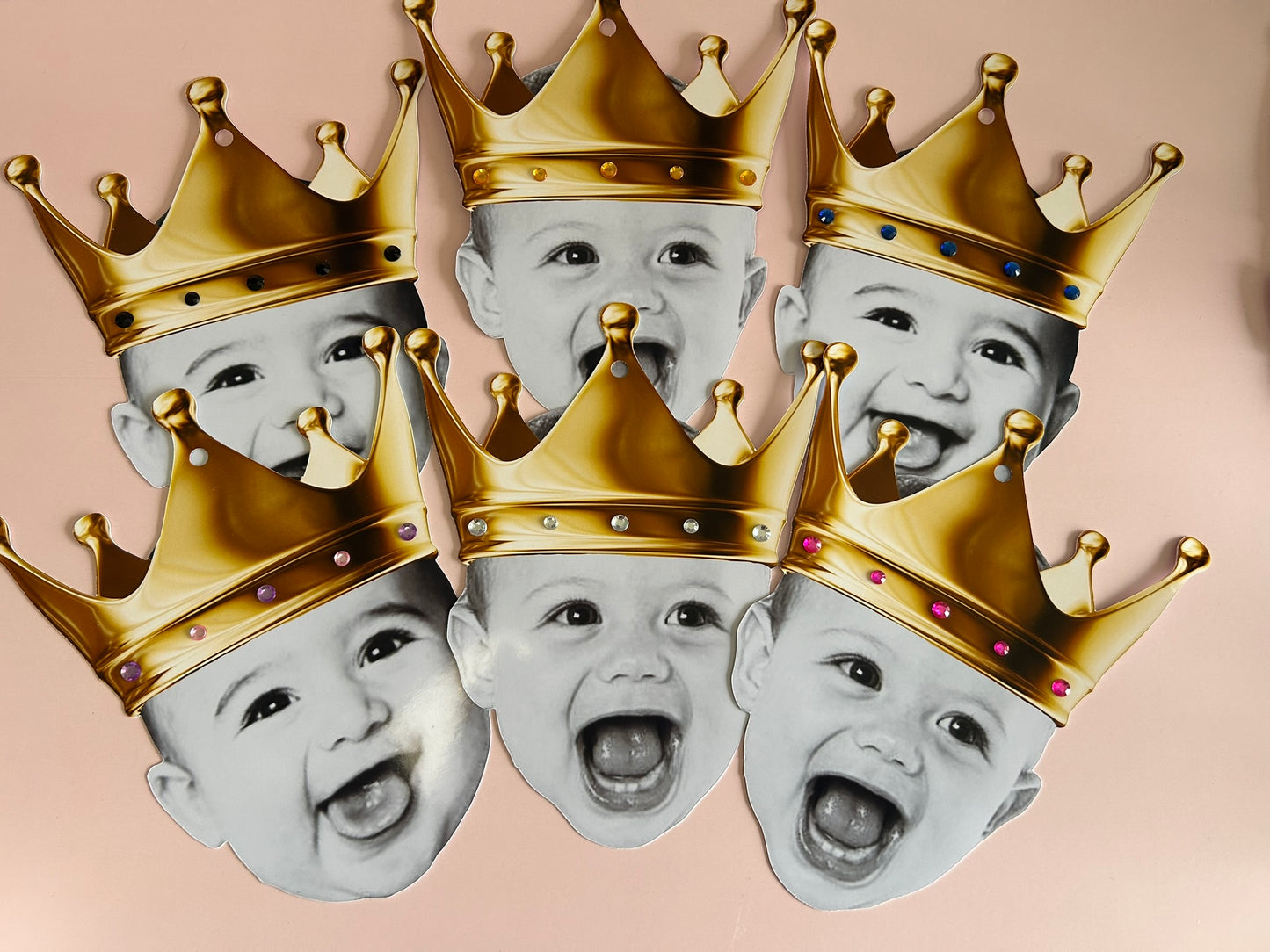 Five baby faces wearing gold crowns on a pink background