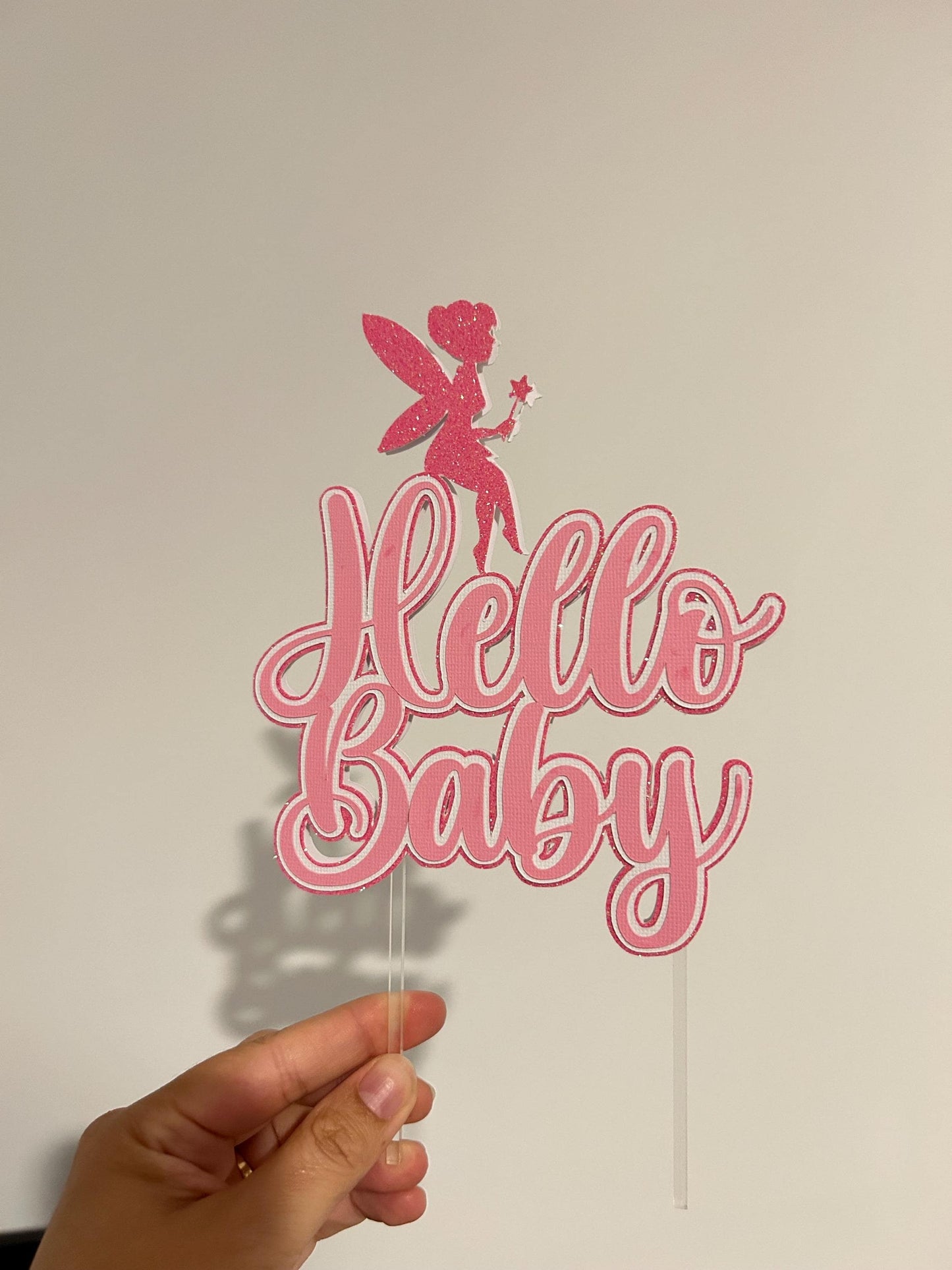 Pink 'Hello Baby' cake topper with a fairy design held against a plain background.