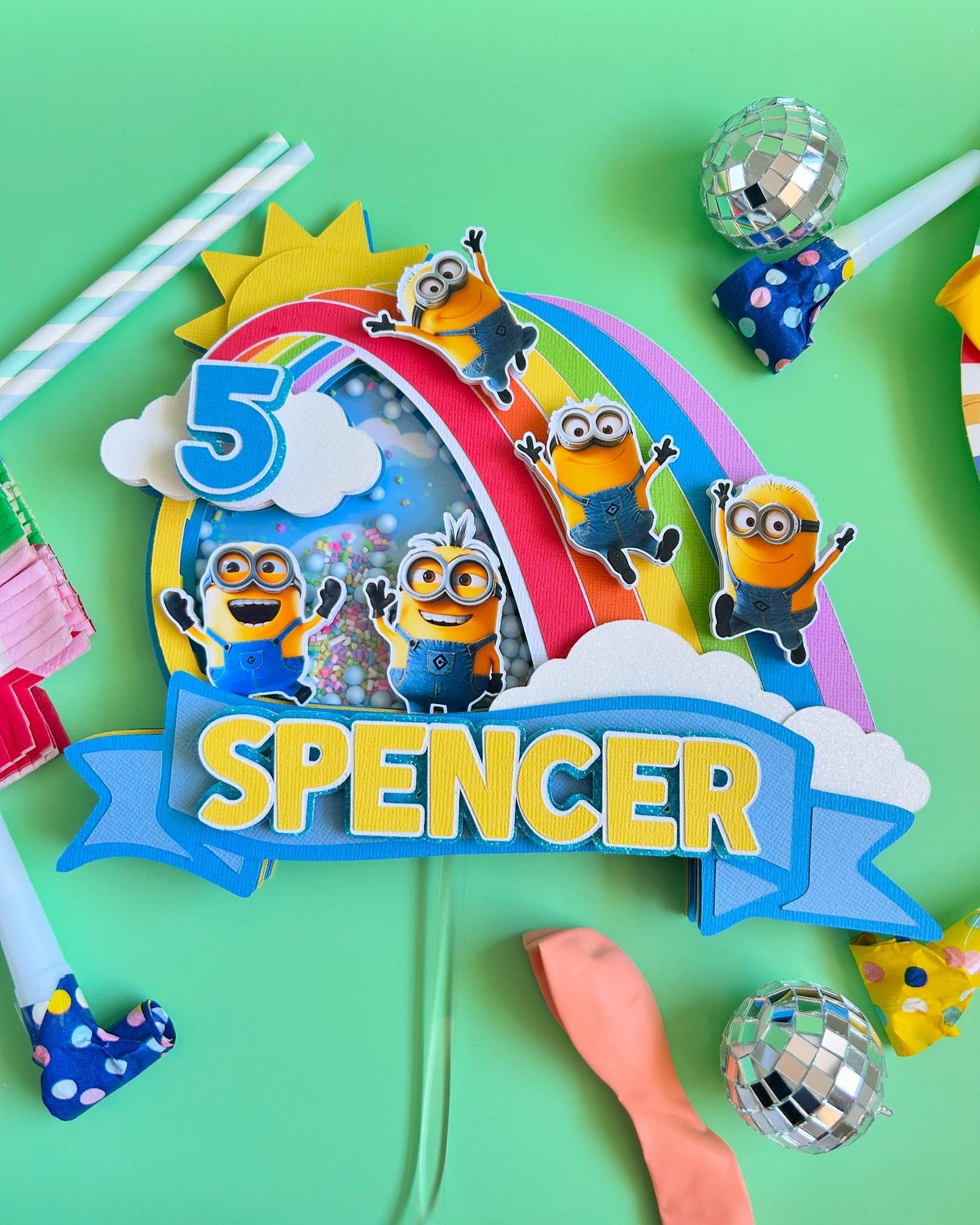Colorful birthday cake topper with Minions, number 5, and name 'Spencer' on a green background.